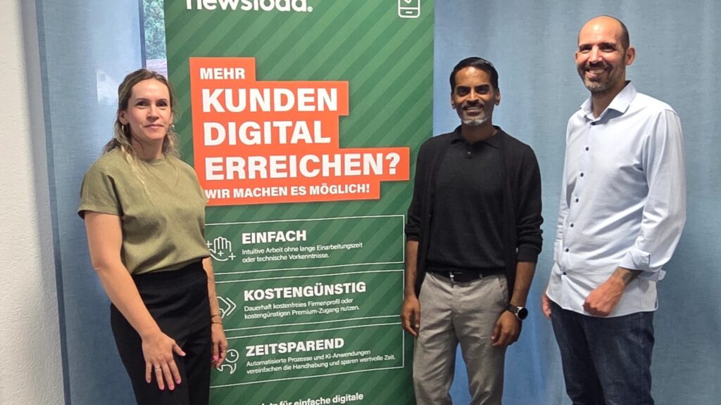 Drei erwachsene Personen (zwei Männer, eine Frau) stehen nebeneinander vor einem grünen Werbebanner mit dem Text „Mehr Kunden digital erreichen?“.